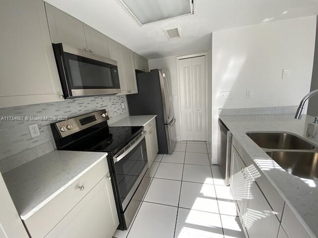 kitchen featuring sink, tasteful backsplash, light tile patterned floors, appliances with stainless steel finishes, and light stone countertops