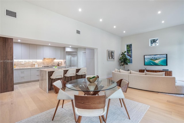 dining room with sink, a towering ceiling, and light hardwood / wood-style flooring