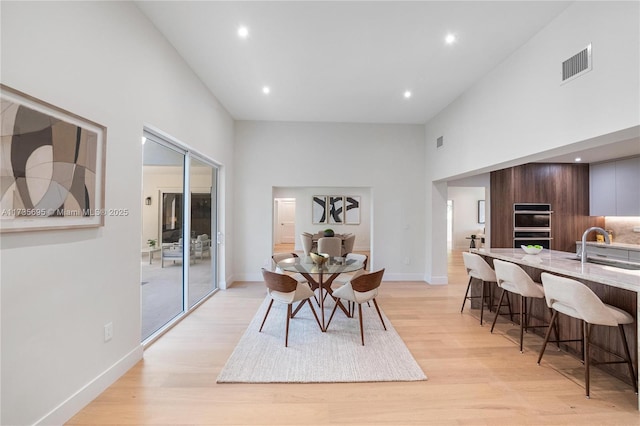 dining area featuring sink, light hardwood / wood-style flooring, and a high ceiling