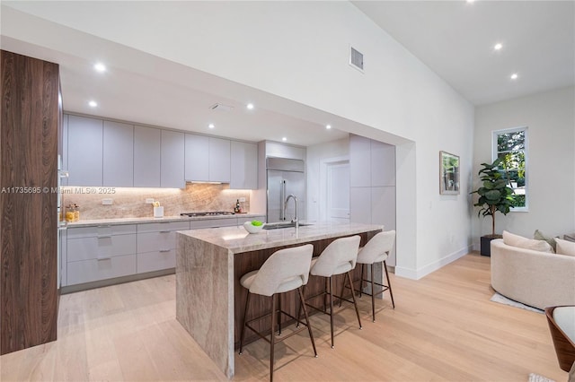 kitchen featuring a kitchen bar, sink, gray cabinetry, appliances with stainless steel finishes, and a large island