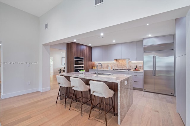 kitchen featuring appliances with stainless steel finishes, sink, a kitchen breakfast bar, a kitchen island with sink, and light stone counters