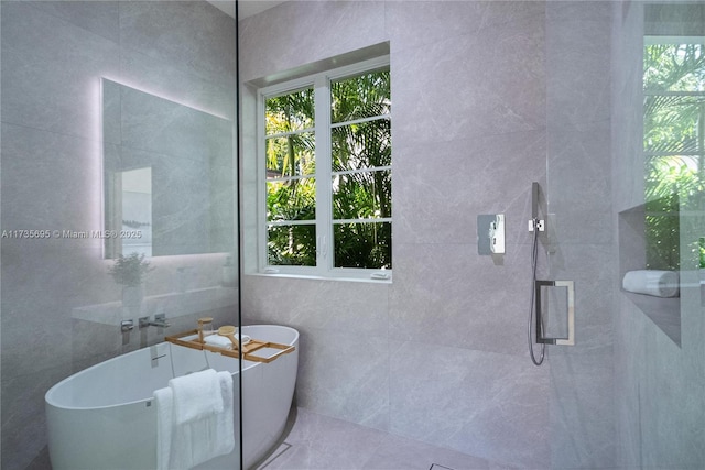 bathroom with tile walls, a wealth of natural light, and separate shower and tub