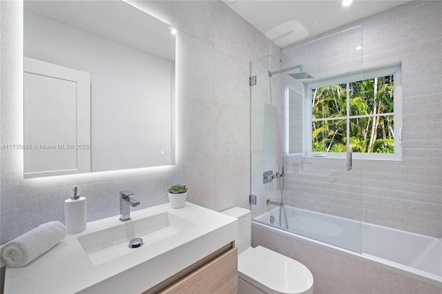 full bathroom featuring combined bath / shower with glass door, tile walls, vanity, decorative backsplash, and toilet