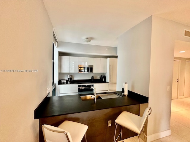 kitchen featuring light tile patterned floors, a breakfast bar area, white cabinetry, kitchen peninsula, and oven