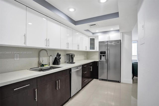 kitchen with dark brown cabinetry, sink, appliances with stainless steel finishes, a raised ceiling, and white cabinets