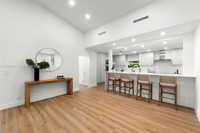 kitchen with a kitchen bar, white cabinetry, high vaulted ceiling, light wood-type flooring, and kitchen peninsula