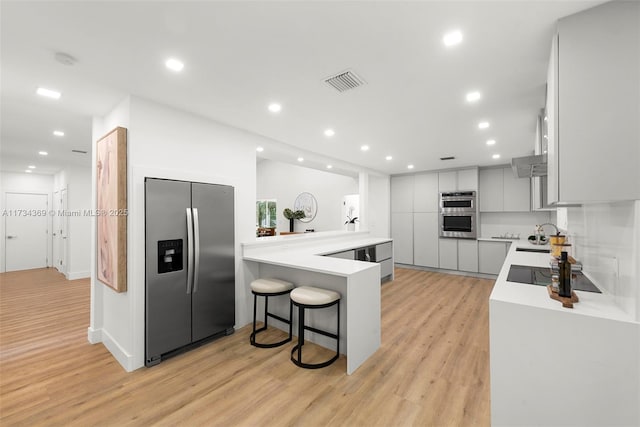 kitchen with a breakfast bar area, light wood-type flooring, kitchen peninsula, stainless steel appliances, and white cabinets