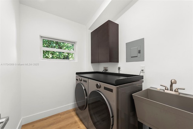 laundry room featuring sink, electric panel, washer and clothes dryer, and light hardwood / wood-style flooring