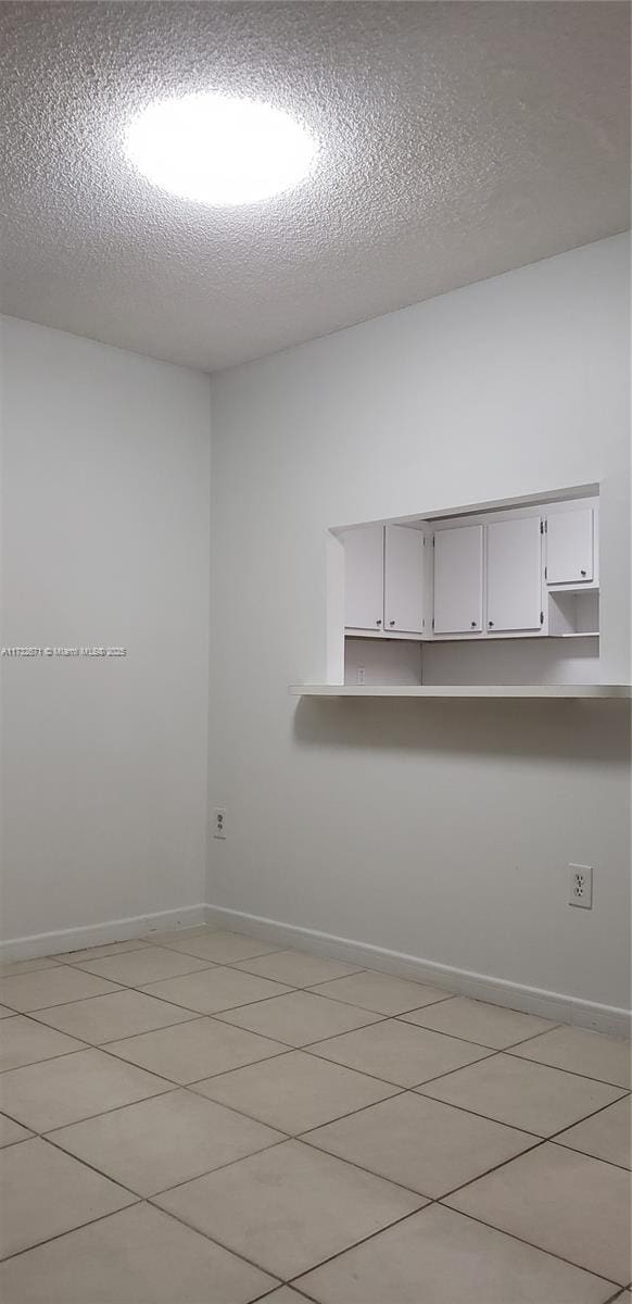 unfurnished room with light tile patterned floors, baseboards, and a textured ceiling