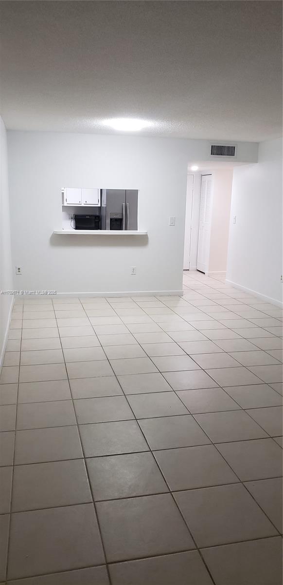 empty room with light tile patterned floors, visible vents, and baseboards