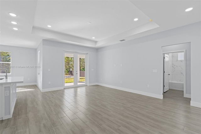 unfurnished living room featuring a tray ceiling, light hardwood / wood-style flooring, and french doors