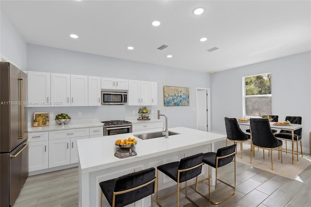 kitchen featuring an island with sink, appliances with stainless steel finishes, sink, and white cabinets