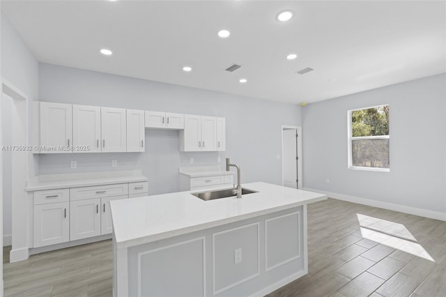 kitchen with sink, light wood-type flooring, an island with sink, light stone countertops, and white cabinets