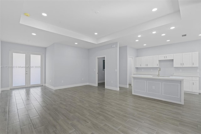 unfurnished living room with french doors, a raised ceiling, and sink