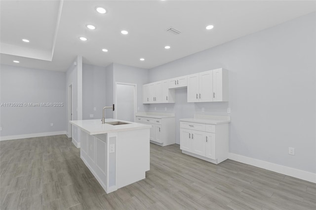 kitchen with a kitchen island with sink, sink, white cabinets, and light hardwood / wood-style flooring