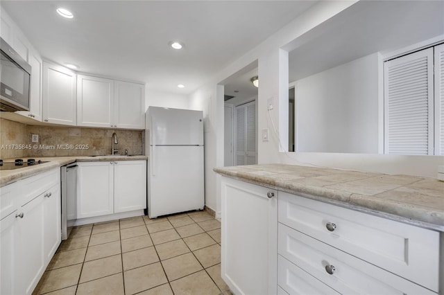 kitchen with light tile patterned flooring, tasteful backsplash, white cabinetry, sink, and white fridge