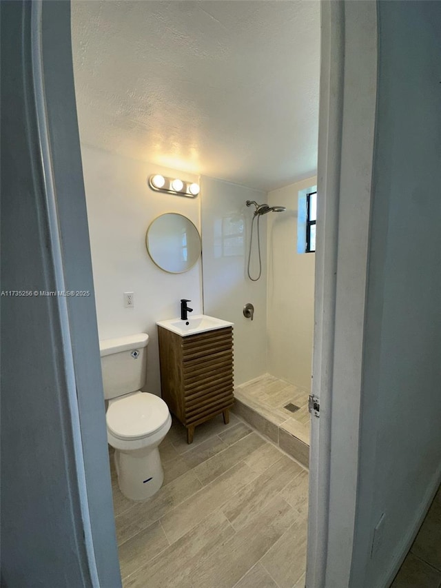 bathroom with vanity, toilet, a textured ceiling, and a tile shower