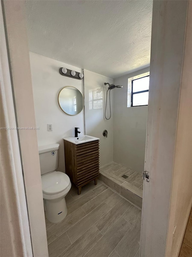 bathroom featuring tiled shower, vanity, toilet, and a textured ceiling