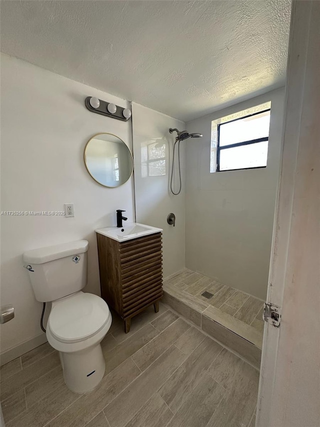 bathroom featuring vanity, a tile shower, a textured ceiling, and toilet