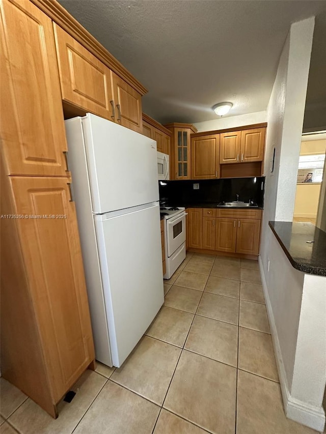 kitchen featuring sink, dark stone countertops, light tile patterned floors, white appliances, and a textured ceiling