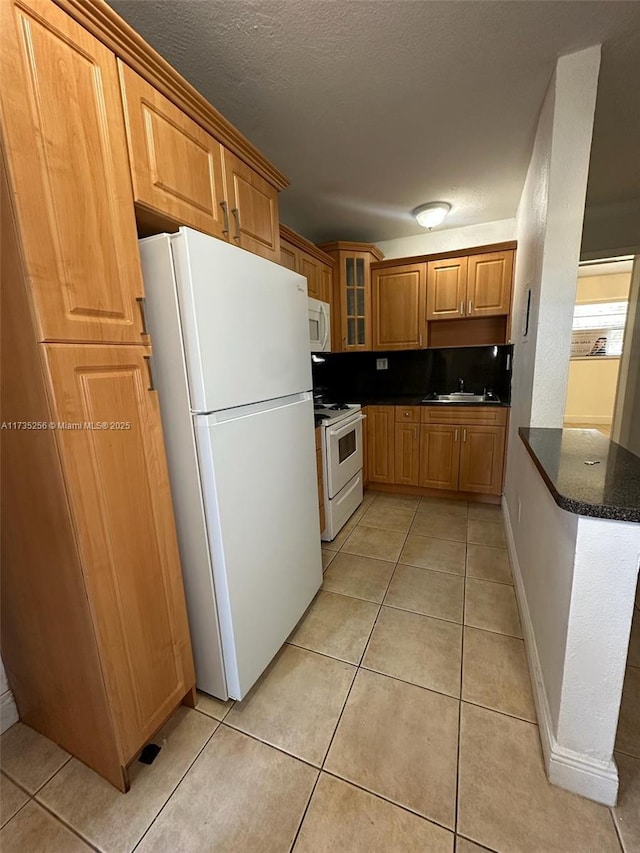 kitchen with sink, light tile patterned floors, white appliances, and dark stone counters