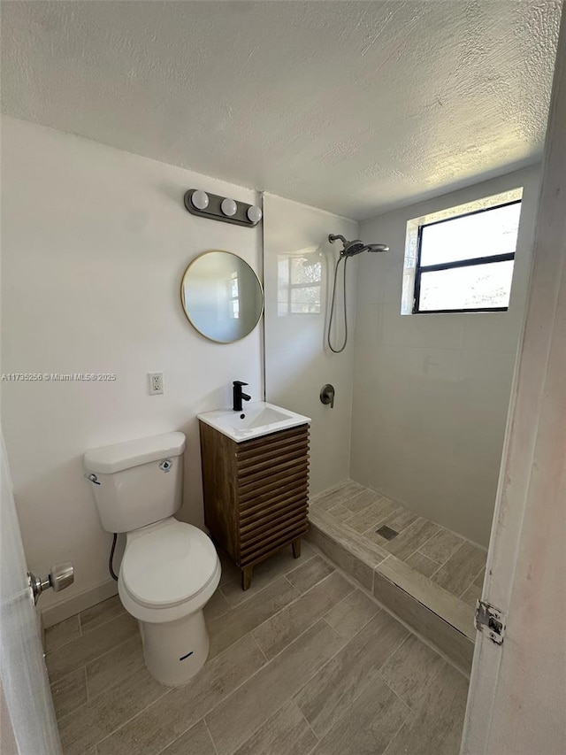 bathroom with a tile shower, vanity, a textured ceiling, and toilet