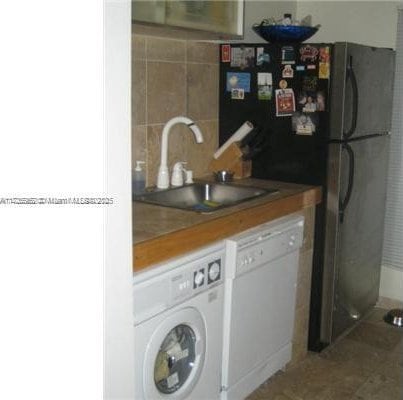 kitchen featuring washer / dryer, sink, wooden counters, and white dishwasher