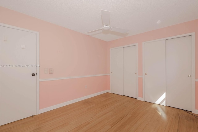 unfurnished bedroom with ceiling fan, two closets, a textured ceiling, and hardwood / wood-style flooring