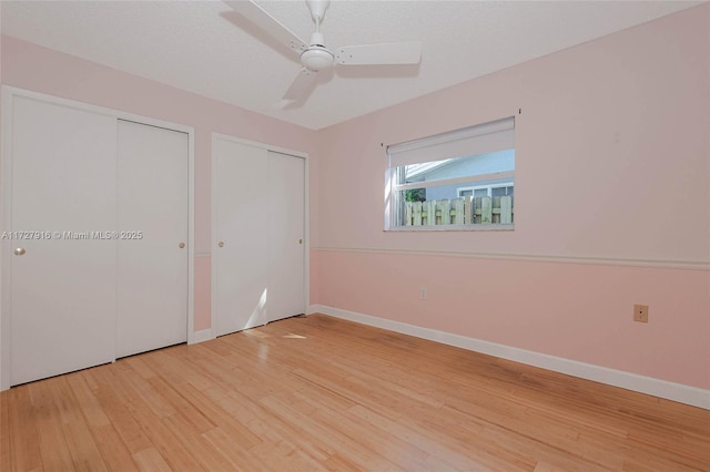 unfurnished bedroom with ceiling fan, two closets, a textured ceiling, and light wood-type flooring