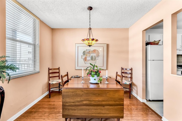 dining space featuring light wood-style flooring, a textured ceiling, and baseboards