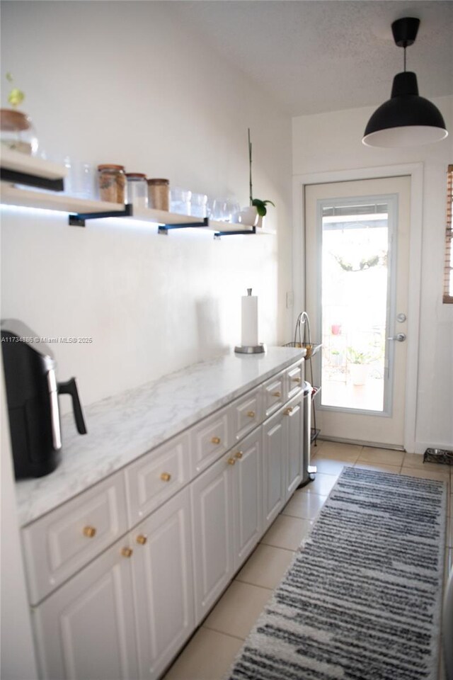 kitchen featuring decorative light fixtures, white cabinets, light tile patterned floors, light stone counters, and a textured ceiling