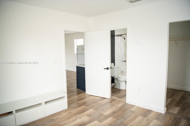 unfurnished bedroom with white refrigerator, a spacious closet, hardwood / wood-style floors, and a closet