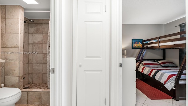 bathroom featuring tile patterned flooring, toilet, and tiled shower