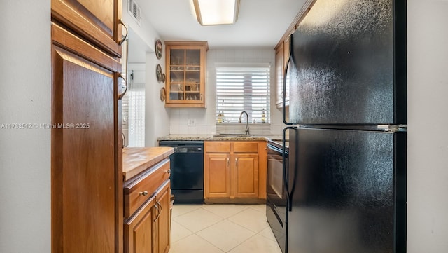 kitchen featuring sink, decorative backsplash, light tile patterned floors, light stone counters, and black appliances