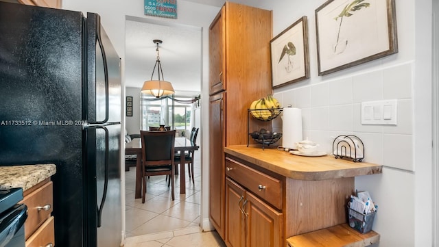 kitchen with black refrigerator, wood counters, decorative light fixtures, backsplash, and light tile patterned floors