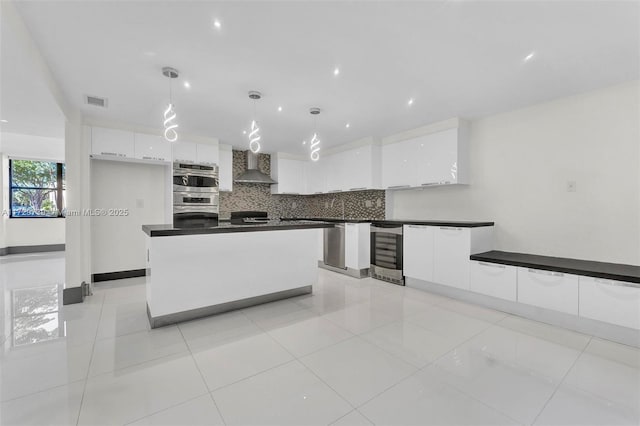 kitchen featuring hanging light fixtures, white cabinets, beverage cooler, and wall chimney exhaust hood