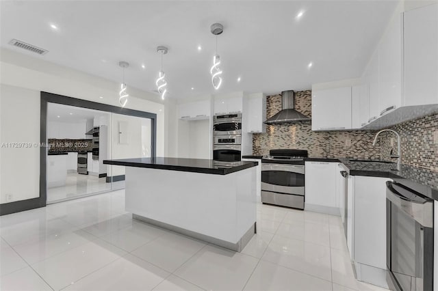 kitchen with wall chimney range hood, sink, white cabinetry, hanging light fixtures, and stainless steel appliances