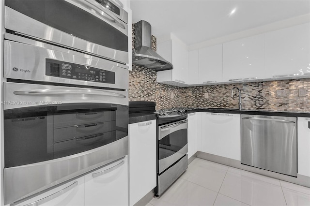 kitchen with light tile patterned floors, white cabinets, stainless steel appliances, decorative backsplash, and wall chimney range hood