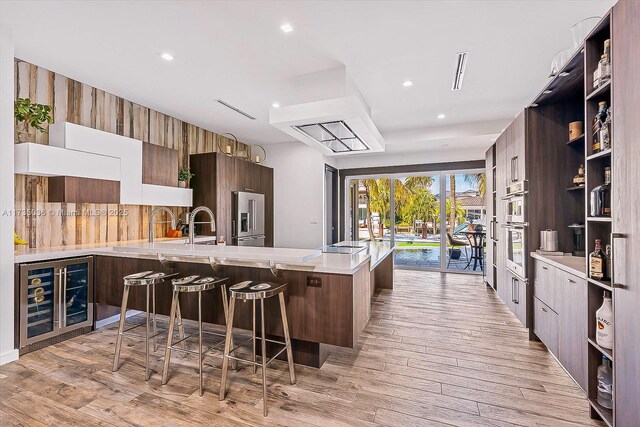 kitchen featuring a kitchen bar, high end refrigerator, light wood-type flooring, kitchen peninsula, and beverage cooler