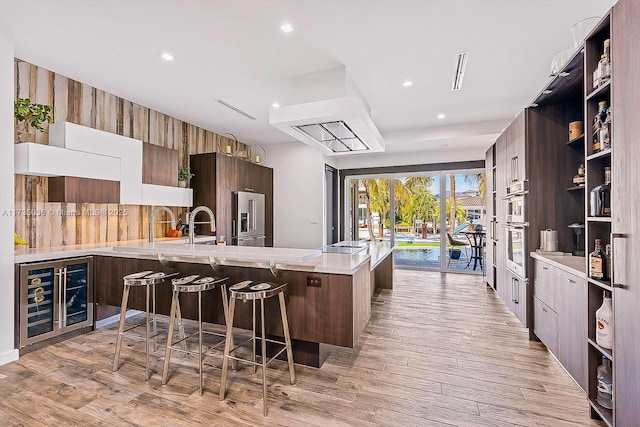 kitchen featuring a kitchen bar, light hardwood / wood-style flooring, beverage cooler, kitchen peninsula, and high end refrigerator