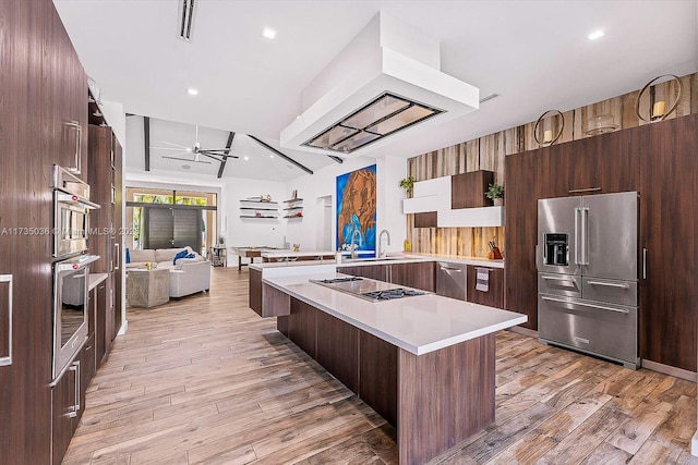 kitchen with premium range hood, a kitchen island, high quality fridge, black electric stovetop, and light wood-type flooring