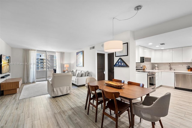 dining space featuring sink, a wall of windows, and light hardwood / wood-style floors