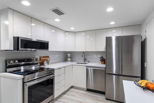 kitchen featuring tasteful backsplash, sink, white cabinets, stainless steel appliances, and light wood-type flooring