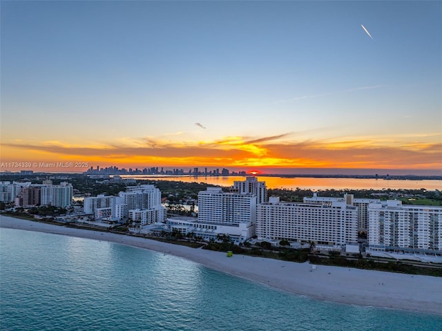 aerial view at dusk with a water view and a view of the beach