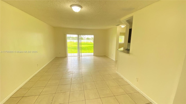 empty room featuring light tile patterned floors, baseboards, and a textured ceiling