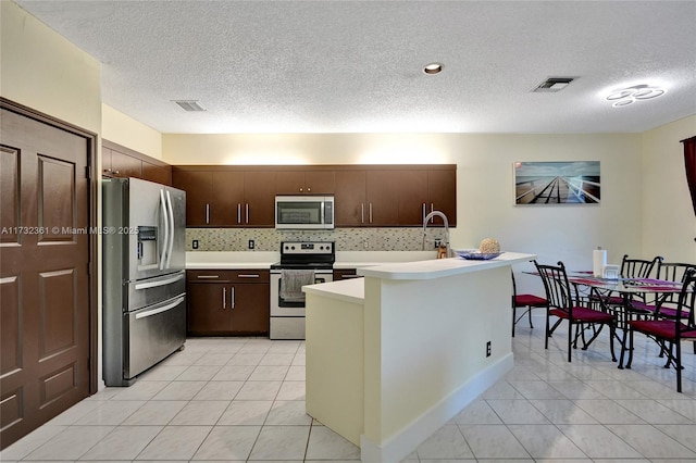 kitchen featuring dark brown cabinetry, appliances with stainless steel finishes, decorative backsplash, and light tile patterned floors