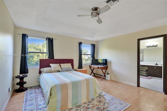 bedroom featuring ceiling fan, ensuite bath, light hardwood / wood-style flooring, and a textured ceiling