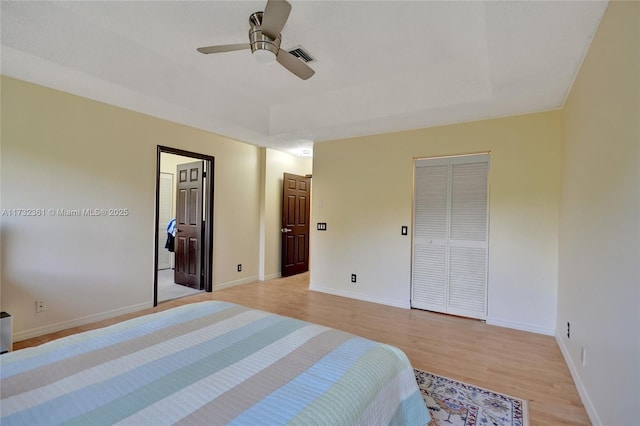 bedroom with ceiling fan, a closet, a raised ceiling, and light hardwood / wood-style flooring