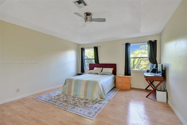 bedroom featuring multiple windows, light hardwood / wood-style floors, and a raised ceiling