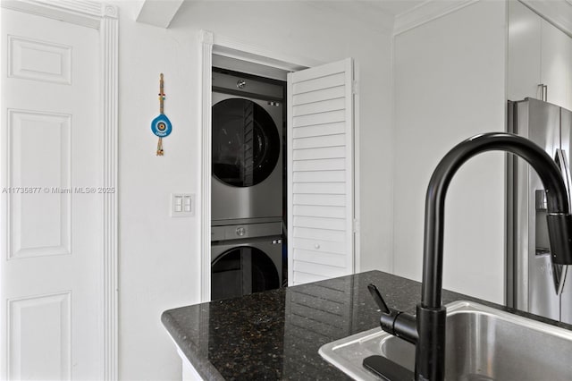 kitchen featuring stacked washing maching and dryer, sink, dark stone countertops, and ornamental molding